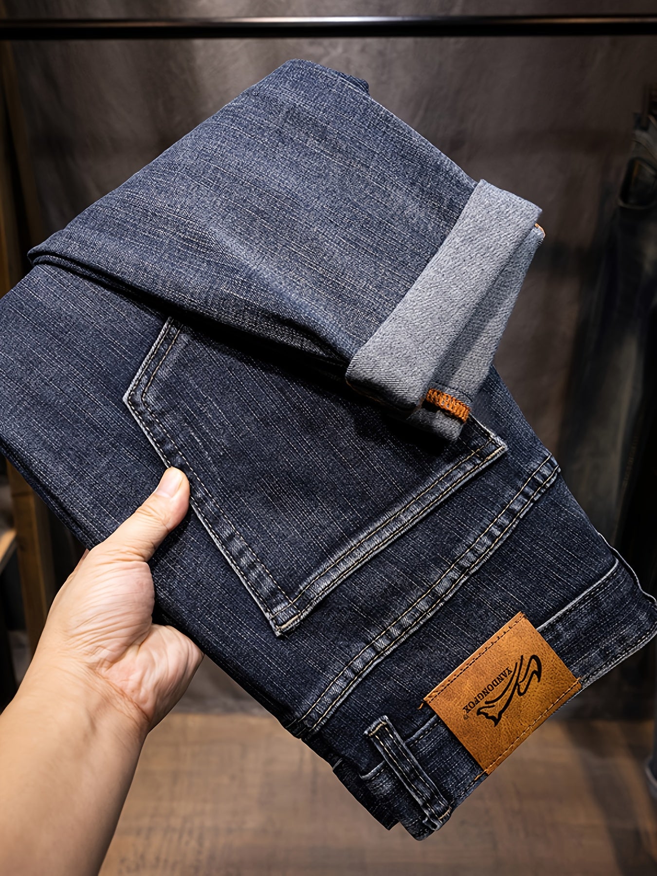 Folded blue jeans held by a hand with a brand label on a blurred background